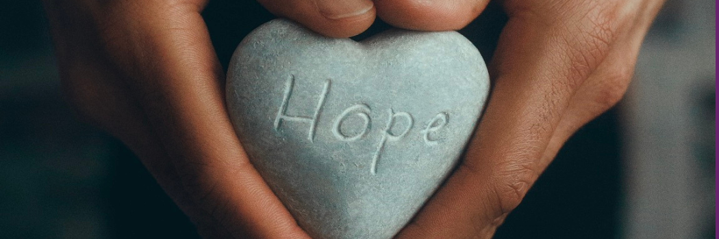 Hands holding a stone with the word 'Hope' engraved on it.