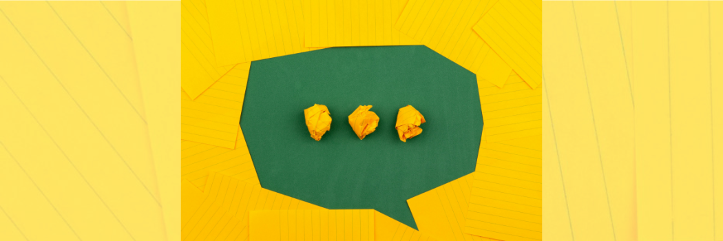 A green speech bubble on a background of yellow lined paper with three crumpled yellow balls inside