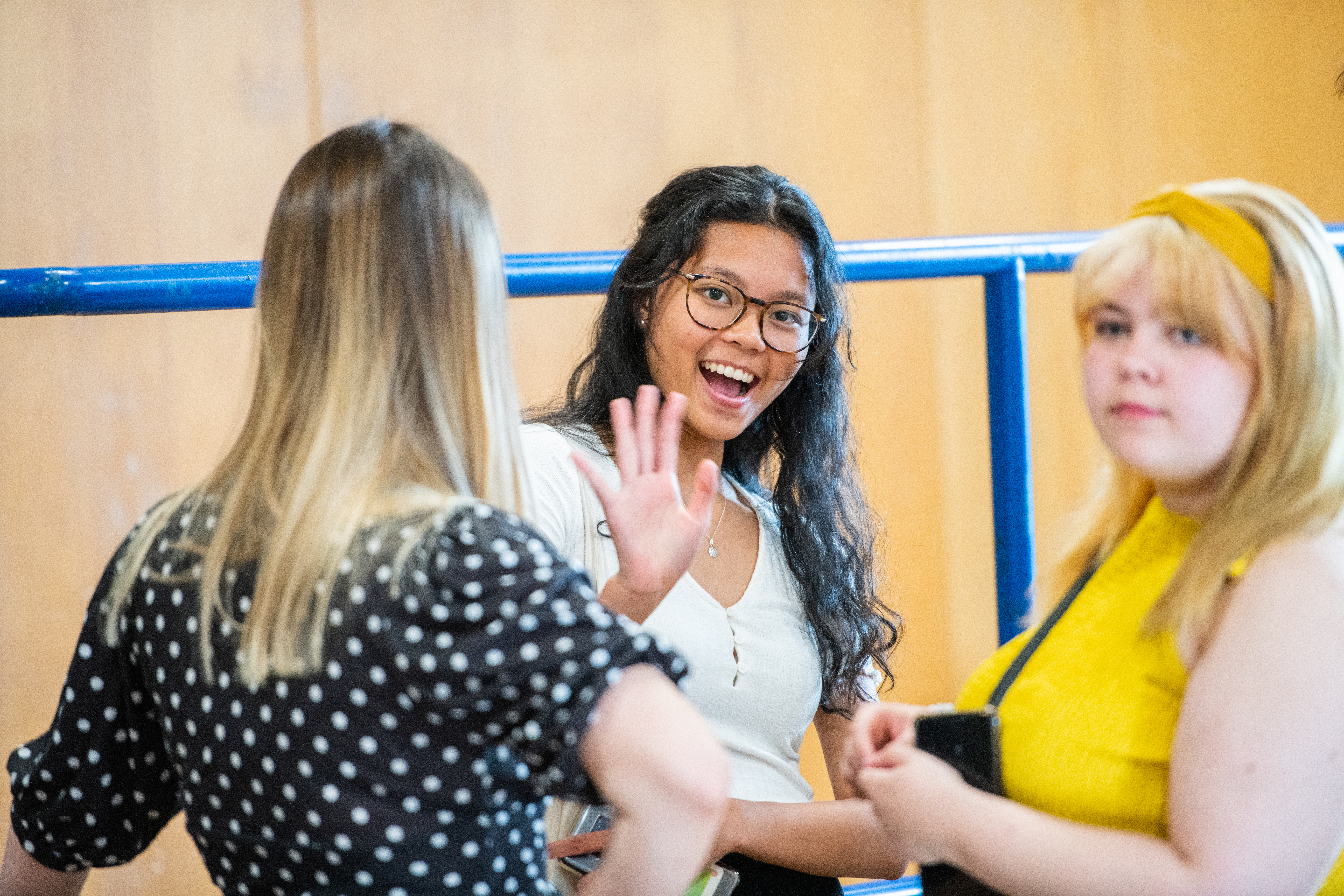Three students with one smiling and waving at the camera