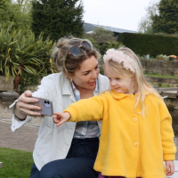 A mother and child in the Botanic Garden looking at a mobile phone screen and smiling. The child is pointing to the phone screen.