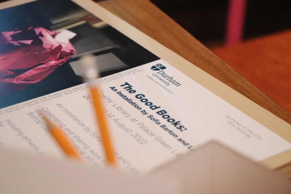Close-up detail of the opening invitation for ‘The Good Books’ art installation, a pot with pencils is in the foreground, out of focus.