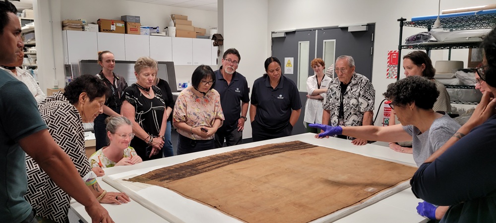 A group of people stand around a table looking at a historic woven cloak