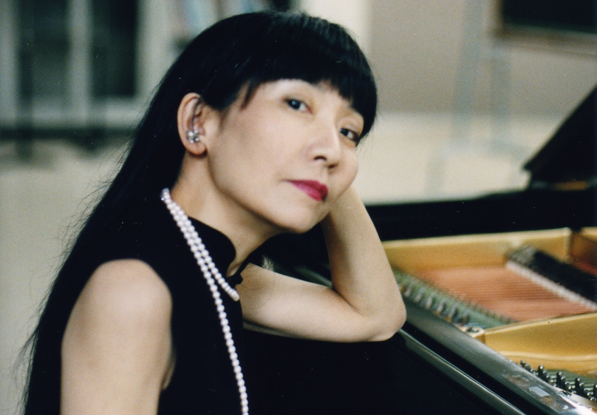 Japanese woman dressed in black wearing a pearl necklace seated at a piano