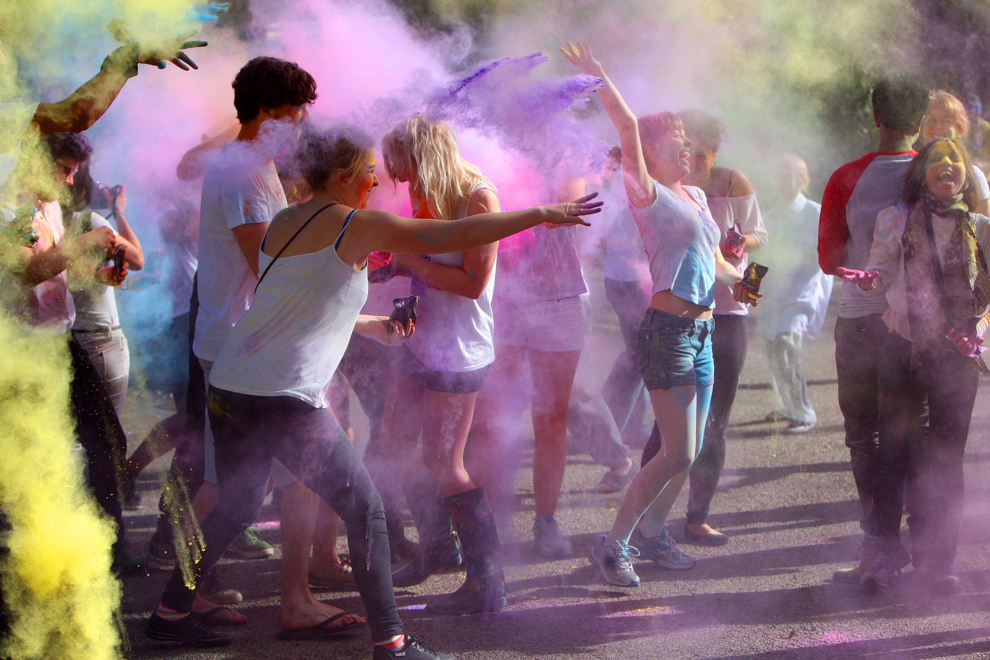 A group of people through multicoloured holi powder into the air and at each other. they are surrounded by a colourful dust cloud of holi powder.