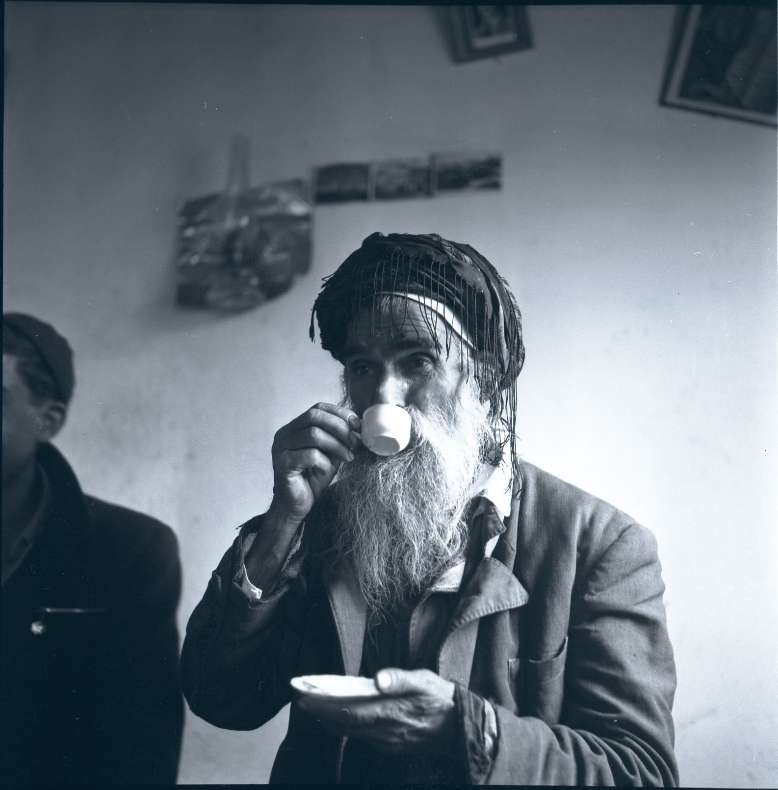 A man with a long beard takes a drink from a mug.